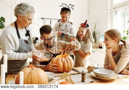 Happy Multi Generational Family Smiling And Carving Jack O Lantern From Pumpkin While Gathering Arou