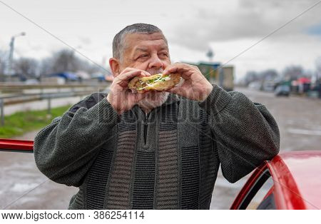 Caucasian Senior Driver Gobbling Lyulya Kebab In Lavash Leaning His Elbow On The Car Roof