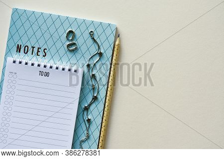 Two Notepads With Pencil, Silver Bracelet And Earrings On A Beige Paper Background. Top View. Close-