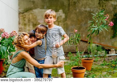 Blond Female Gardener Hugging Her Three Cute Children Son Different Age At Backyard Garden Outdoor. 