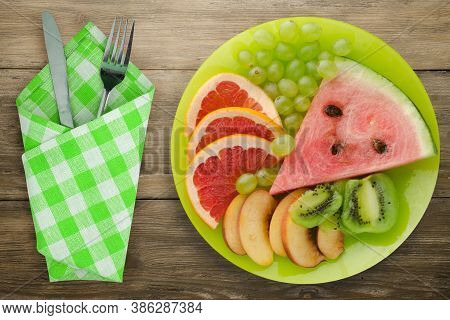 Sliced Fruit On A Borwn Wooden Background. Sliced Fruit On A Light Green Plate Fork And Knife Top Vi