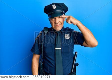 Handsome middle age mature man wearing police uniform pointing unhappy to pimple on forehead, ugly infection of blackhead. acne and skin problem 