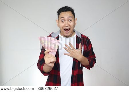 Portrait Of Happy Young Indonesian Man Holding Rupiah Money, Smiling Laughing Winning Gesture, Over 