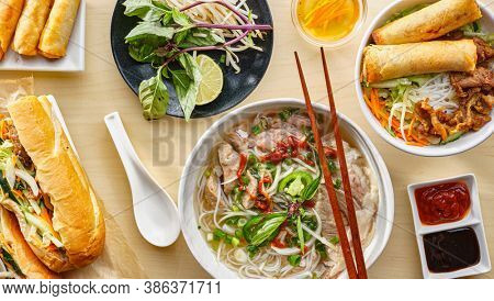 assorted vietnamese dishes with pho, bahn mi, spring rolls in top down composition on dinner table