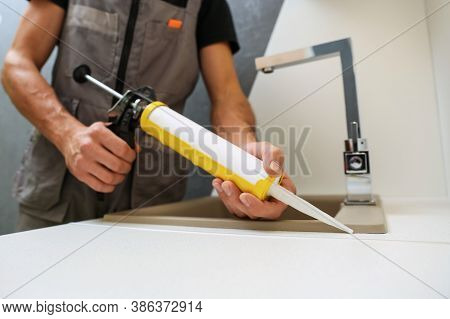 Worker Seals Kitchen Sink With Sealant. Hands Of Worker Works With Construction Sealant Gun In The K