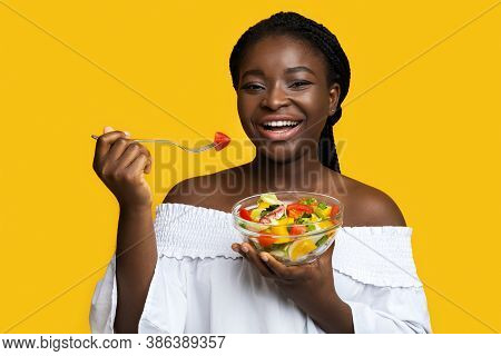 Healthy Nutrition. Happy Black Young Woman Eating Fresh Vegetable Salad With Fork, Holding Bowl With