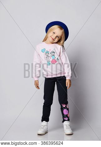 Full-growth Portrait Of Blonde Kid Girl In Gray Sweatshirt Sweater, Blue Pants And Sneakers Standing