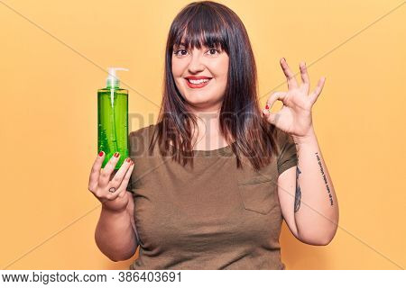 Young plus size woman holding aloe vera doing ok sign with fingers, smiling friendly gesturing excellent symbol 
