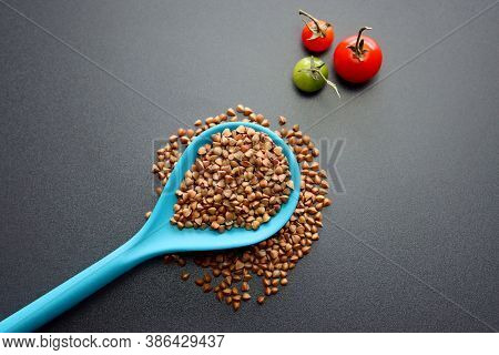 Buckwheat In A Blue Spoon On A Gray Background.