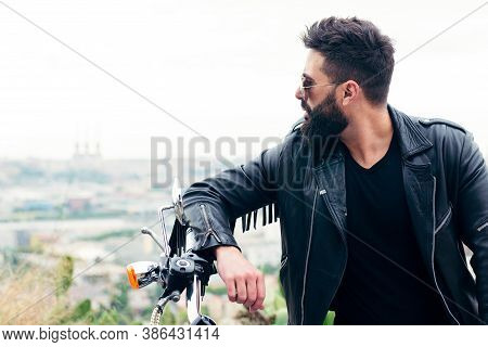 Portrait Of A Bearded Man In A Leather Jacket Leaning Against The Handlebars Of His Motorcycle, Conc