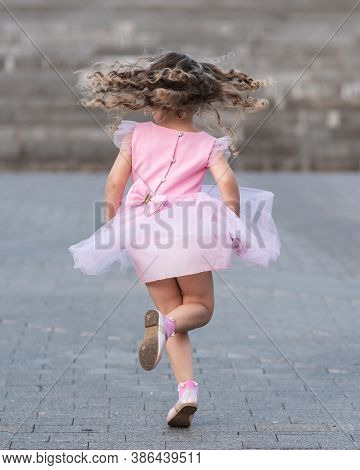 Little Girl In Pink Dress Spinning Around On The Street. Back View