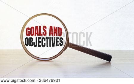 Magnifying Glass With Text Goals And Objectives On Wooden Table.
