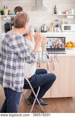 Senior Couple Saying Hello To Daughter And Niece. Happy Senior Woman During A Video Conference With 