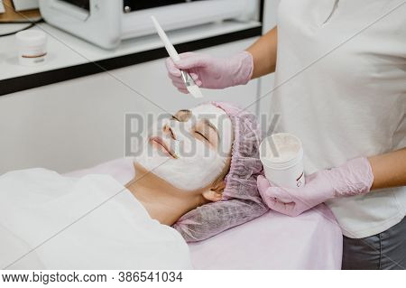 Professional Esthetician Apply Face Mask To The Clients Face In Spa Beauty Center. Young Woman Getti