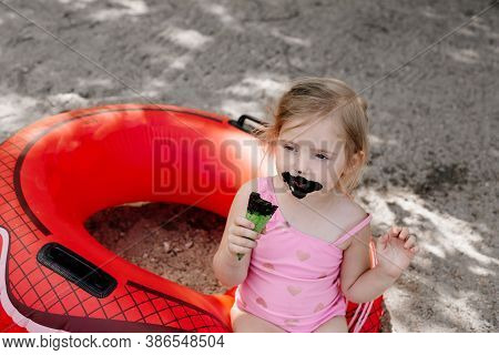 Little Girl Eating Black Ice Cream On The Beach. Lifebuoy. Dirty Child. High Quality Photo