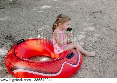 Little Girl Eating Black Ice Cream On The Beach. Lifebuoy. Dirty Child. High Quality Photo