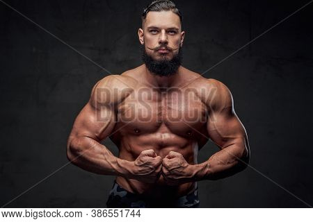 Brutal Military Athlete With Naked Torso And With Beard And Mustache Posing In Dark Gray Background.
