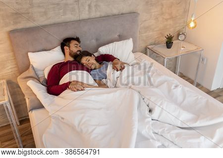 Beautiful Young Couple In Love Wearing Pajams, Lying In Bed Covered With Duvet, Hugging And Sleeping