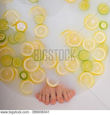 Girl Takes A Milk Bath With Lemons And Limes. Citrus Spa. Body Care. Skin Whitening. Womens Feet.