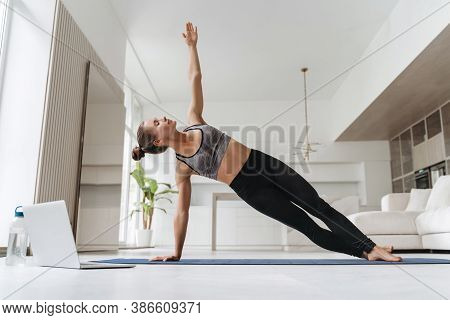 Pretty Girl Wearing Leggings And Short Top Standing In Side Plank On One Hand At Home, Training Body