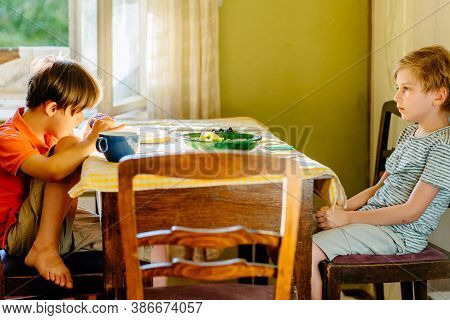 Special Needs Children Concept. Two Children Boy Sitting In Front Of Each Other At Kitchen Table. Be