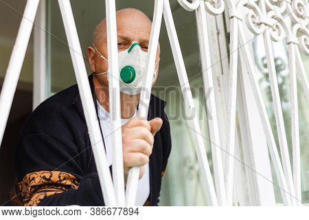 Old Elderly Man In Protective Face Mask Against Virus Looks Out Through Window Stay At Home For Heal