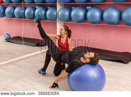 Young Man Helped By His Coach Doing Stretching Exrcises With A Fitness Ball In A Gym.