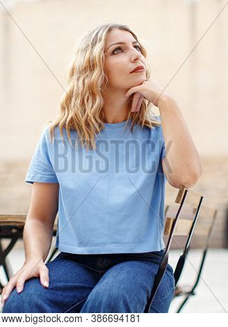 Young Women Wearing T-shirt And Jeans Sits In A Street  Cafe