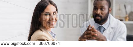 Panoramic Shot Of Joyful Brunette Woman Looking At Camera Near African American Doctor