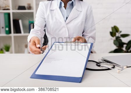 Cropped View Of Doctor Holding Insurance Claim Form Near Stethoscope On Desk