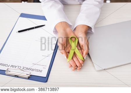 Cropped View Of Psychologist Holding Green Awareness Ribbon Near Insurance Claim Form And Laptop, Me