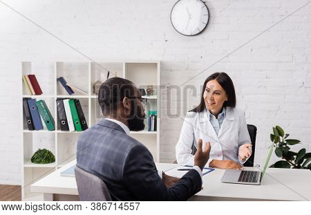 African American Patient And Doctor Painting With Hands Near Laptop At Desk In Hospital