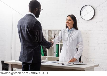 Brunette Woman Shaking Hands With African American Patient Wearing Suit