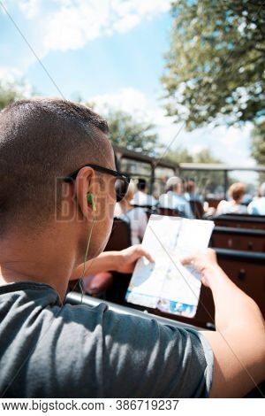 closeup of a young cacausian man traveling on an open top tour bus, checking a city map and using earphones