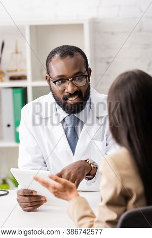 African American Doctor In Eyeglasses Pointing With Finger At Digital Tablet During Conversation Wit