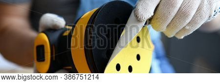 Close-up Of Worker Holding Sander Machine And Changing Disc. Carpenter Working In Protective Gloves.