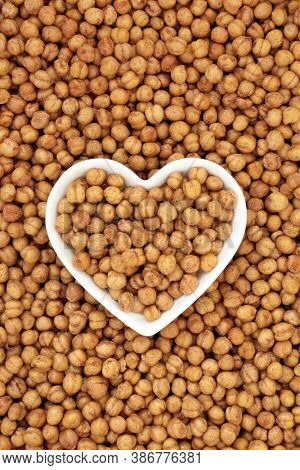 Healthy roasted chickpeas in a porcelain heart shaped bowl forming a background. Vegan & vegetarian health food high in fibre, protein, vitamins and minerals. Flat lay, top view.
