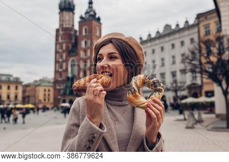 Woman Eating Bagel Obwarzanek Traditional Polish Cuisine Snack On Market Square In Krakow. Travel Eu