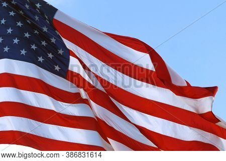 Large American Flag Gently Waving In The Wind. American Flag Waving Under A Blue Sky With Clouds. Re