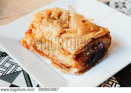Delicious Greek sweet pastry named Galaktoboureko, made of semolina custard in filo, served with honey in white plate.
