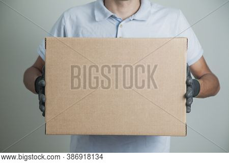 Detail Of Man With Black Gloves Holding A Cardboard Box For Delivering Products On Gray Background. 