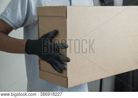 Detail Of Man With Black Gloves Holding A Cardboard Box For Delivering Products On Gray Background. 