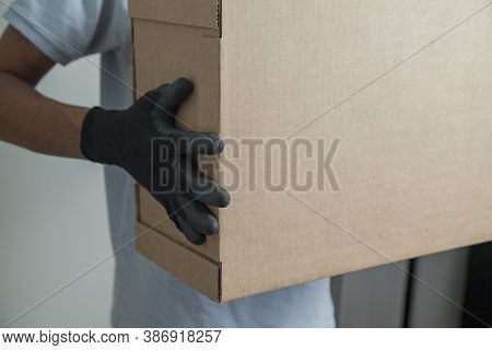 Detail Of Man With Black Gloves Holding A Cardboard Box For Delivering Products On Gray Background. 