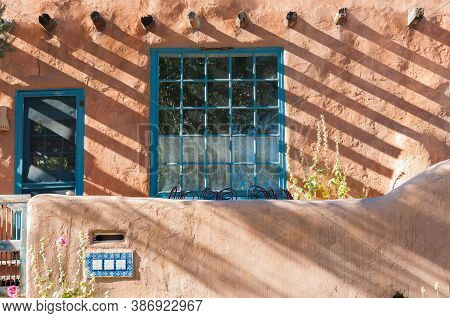 Street View Of Exterior Wall And Blue Window And Shadow Patterns From Beams Beyond Boundary Wall In 
