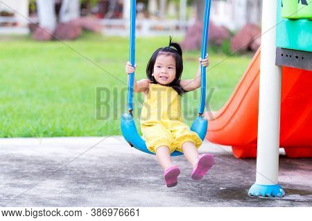 Happy Asian Little Child Girl Aged 3 Years Old Is Playing In A Blue Swing. Children Wearing Yellow J