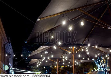 Textile Umbrella With Wooden Frame And Edison String Lights Glowing With White Light On Backyard Ter