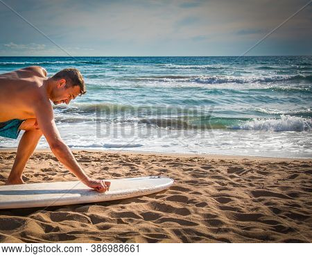 Man Waxing A Surfboard On The Sand Before The Surf Session