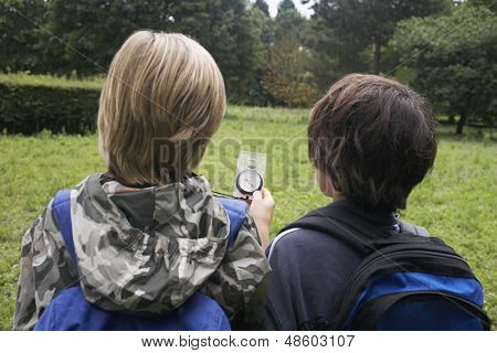 Vista traseira de dois jovens com mochilas usando a bússola