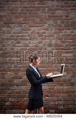 Billede af alvorlige forretningskvinde med laptop gåture langs mur