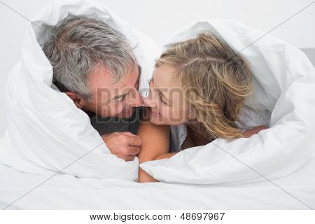 Amantes de media de edad par bajo el edredón frotando narices en dormitorio en casa